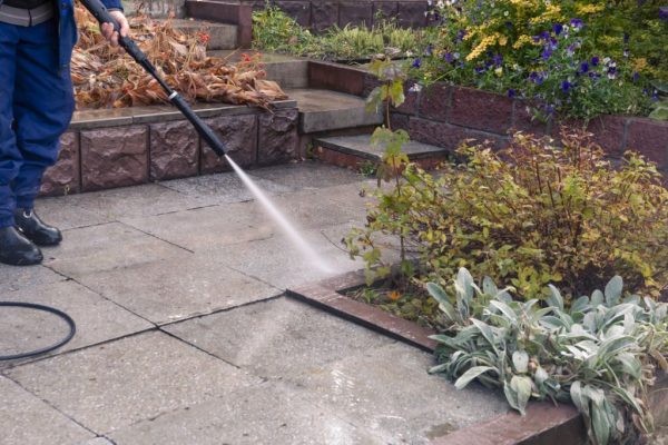 A man washes a garden path with a high pressure washer. Autumn work in the garden.